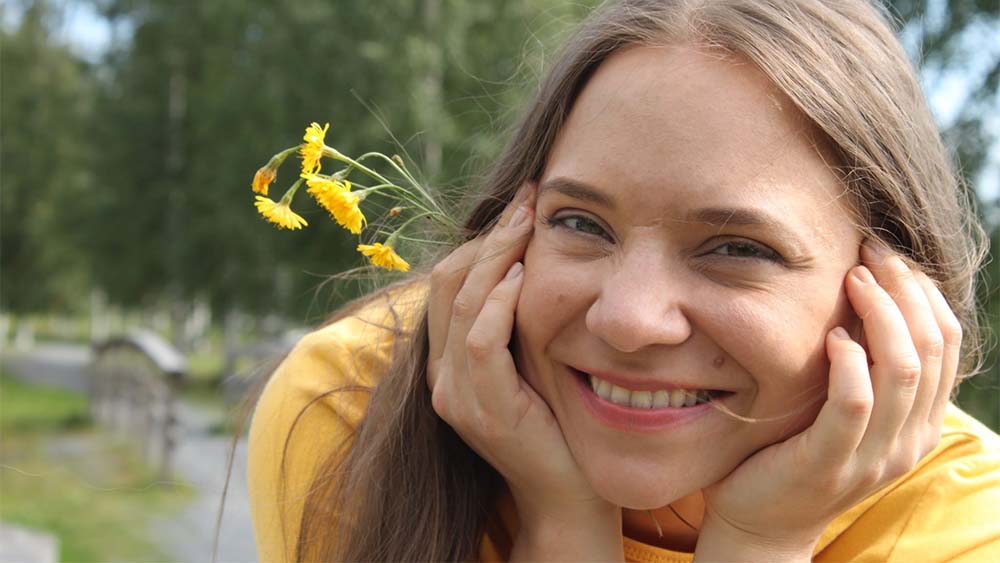Karoliina Fröberg kesäisessä maisemassa keltaisten kukkien kanssa.