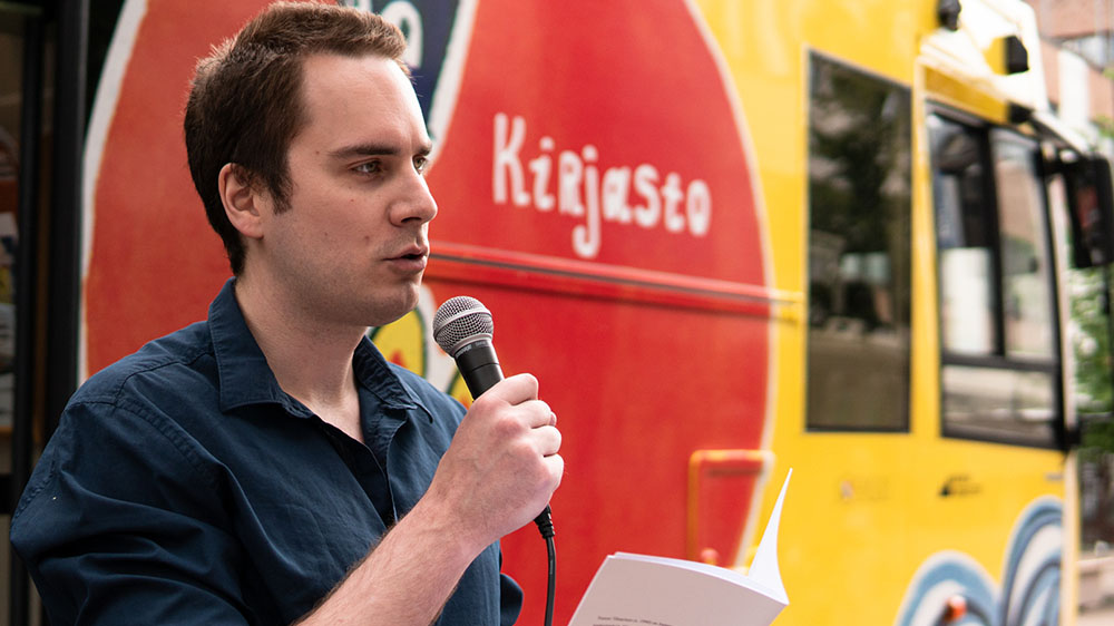 Runokaraoken juontaja Tommi Tihtarinen lukee runoa kirjastoauton edessä, kuvaaja Karoliina Gavrilov.
